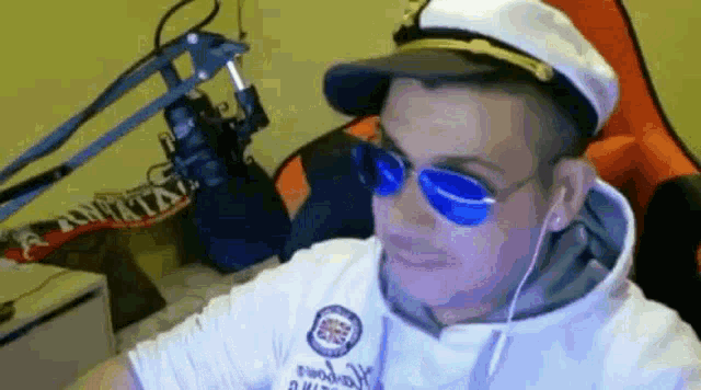 a man wearing a captain 's hat and blue sunglasses is sitting in front of a microphone .