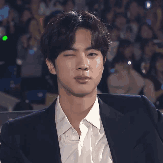 a young man in a suit and white shirt winks at the camera