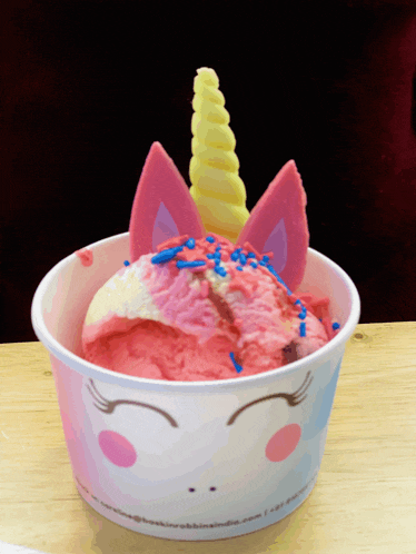 a cup of pink ice cream with a unicorn horn and ears on top