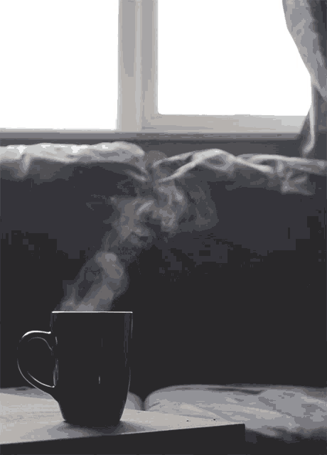 a cup of coffee with steam coming out of it sits on a table in front of a window