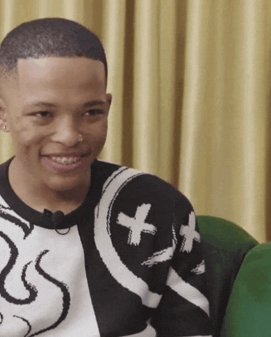 a young man wearing a black and white sweater is smiling while sitting on a couch .