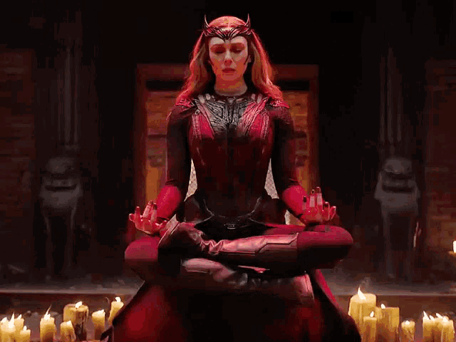 a woman in a red dress is sitting in a lotus position with candles in the background