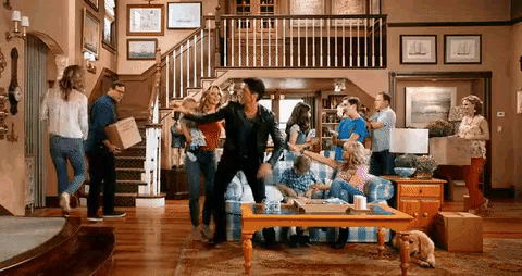 a group of people are dancing in a living room while a dog watches .