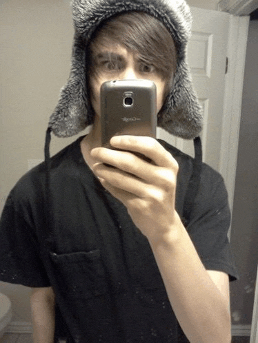 a young man wearing a furry hat takes a selfie with a samsung phone