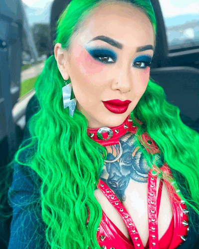 a woman with green hair is wearing a red top with spikes on it