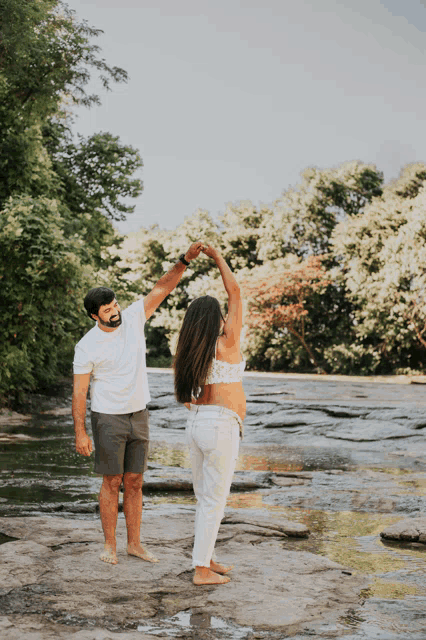 a man and a pregnant woman are dancing on a rock near a river