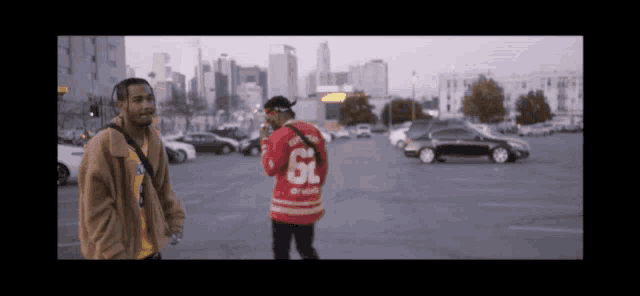 two men are standing in a parking lot with one wearing a red jersey with the number 6 on it