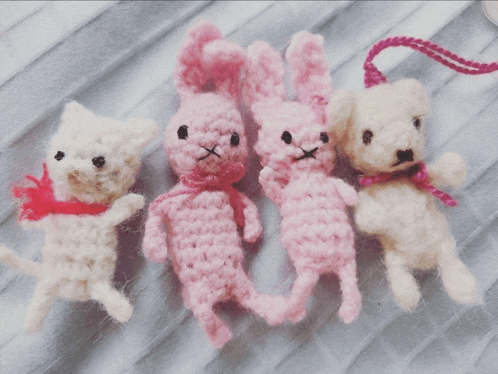 a white cat a pink rabbit and a white teddy bear are sitting on a blanket