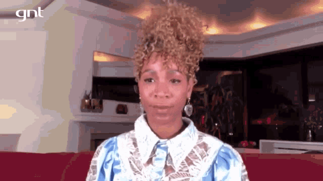 a woman with curly hair is sitting on a red couch in a living room looking at the camera .