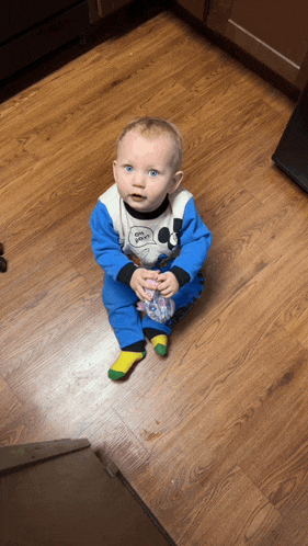 a baby wearing a mickey mouse outfit sits on a wooden floor