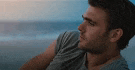 a man in a grey shirt is sitting on the beach looking out at the ocean .