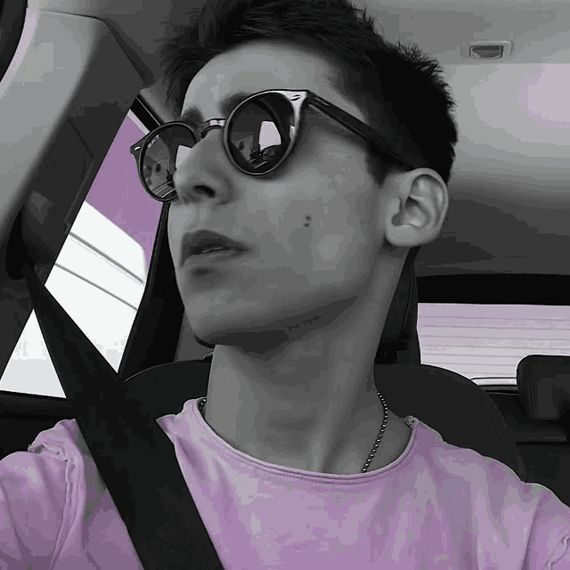 a young man wearing sunglasses and a purple shirt is sitting in a car