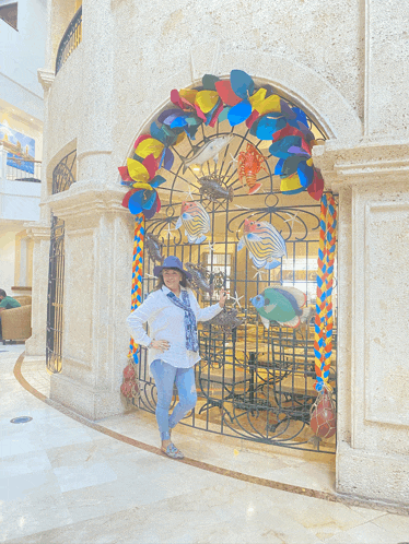 a woman in a hat stands in front of a colorful decoration