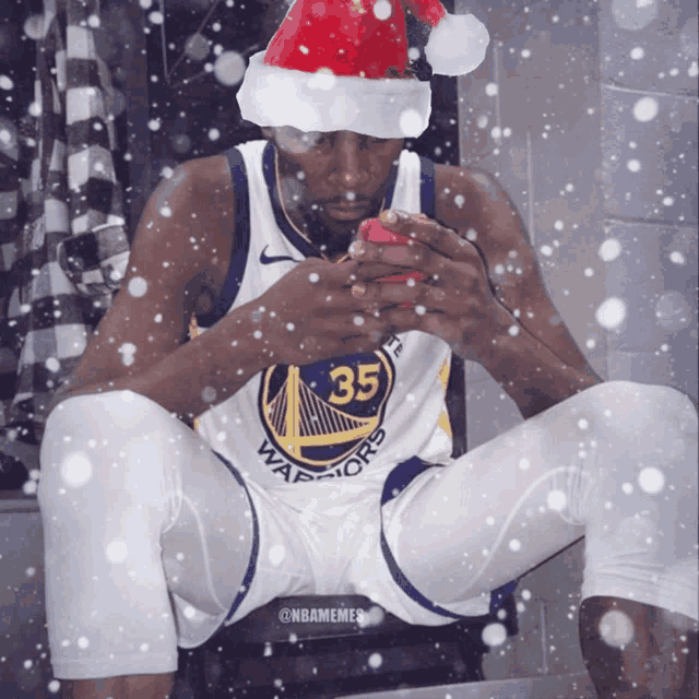 a warriors player wearing a santa hat is looking at his phone