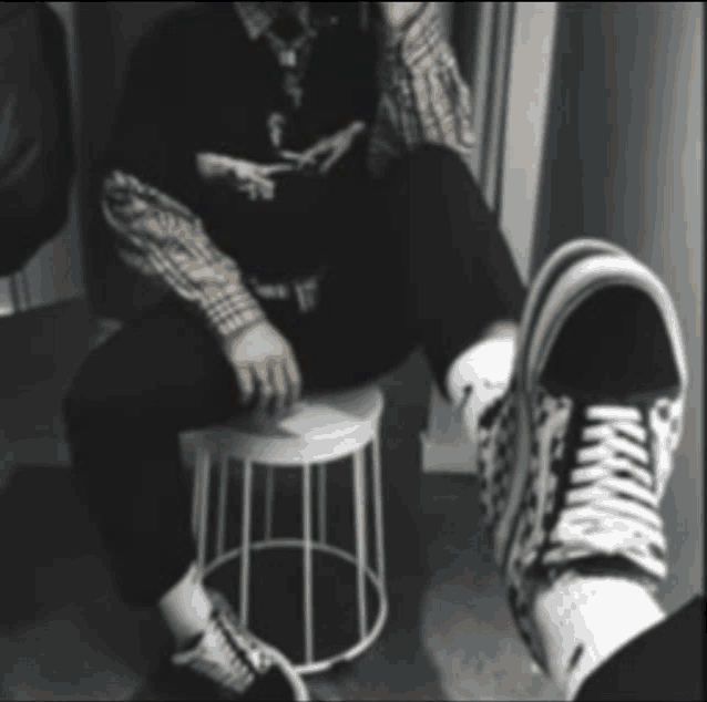 a black and white photo of a person sitting on a stool with their feet in the foreground