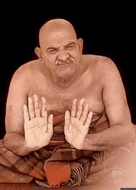 a bald man with a mustache is sitting in a blanket with his hands outstretched