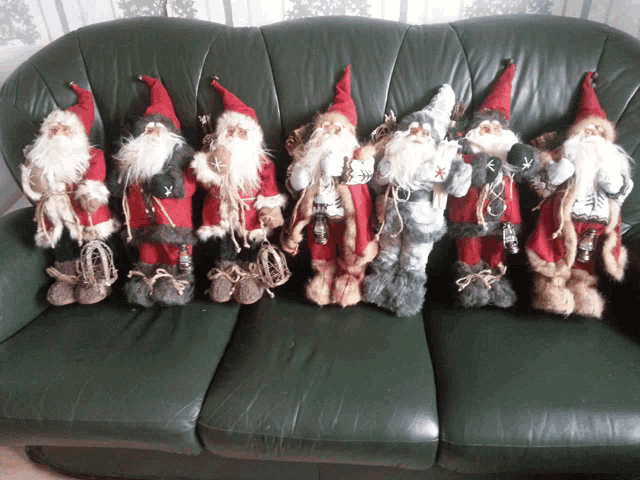 a row of stuffed santa clauses are sitting on a green couch