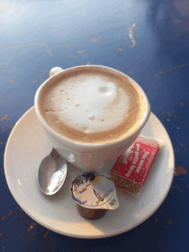 a cup of cappuccino on a saucer with a spoon and a packet of sugar next to it