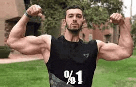 a man in a black tank top is flexing his muscles in front of a building .