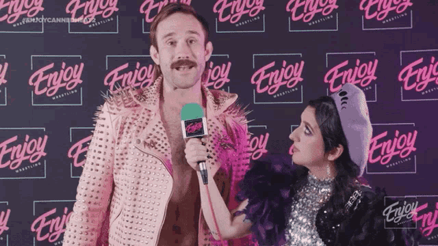 a man in a pink jacket is being interviewed by a woman in front of a backdrop that says enjoy wrestling