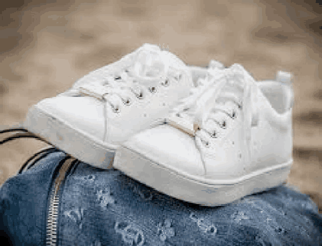 a pair of white sneakers are sitting on top of a blue purse .