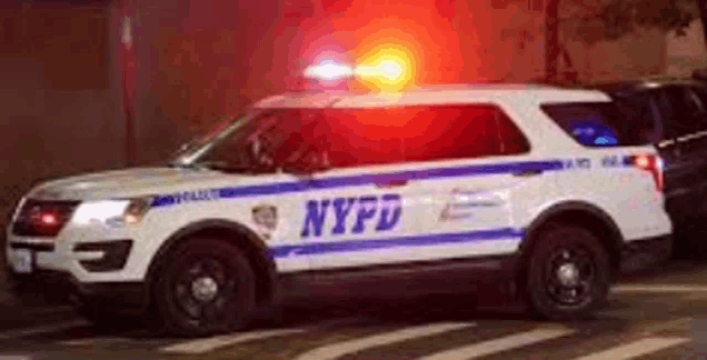 a white and blue nypd police car is driving down the street at night .