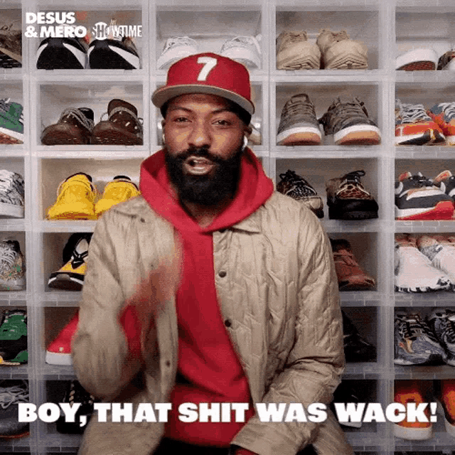 a man with a beard is sitting in front of a wall of shoes and says boy that shit was wack