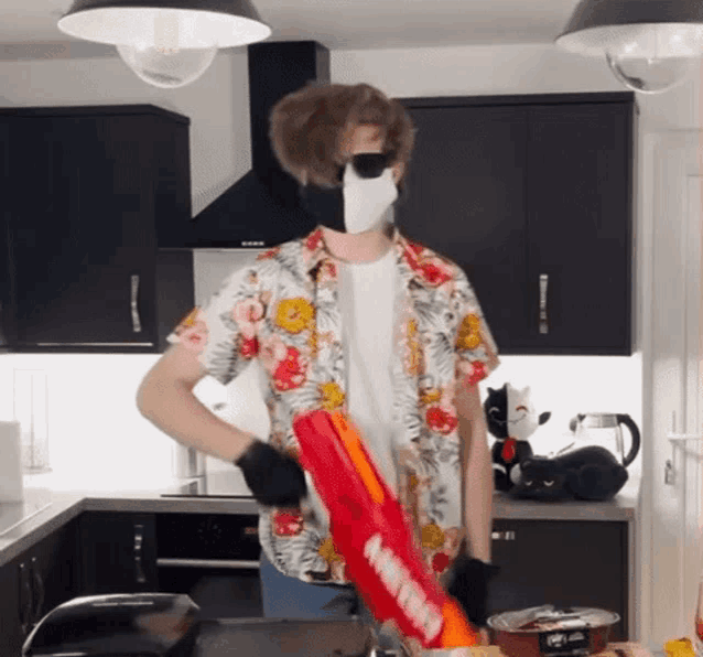 a man wearing a mask is holding a red nerf gun in a kitchen .