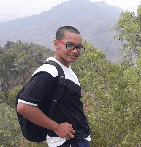 a young man wearing glasses and a backpack stands in front of a mountain range