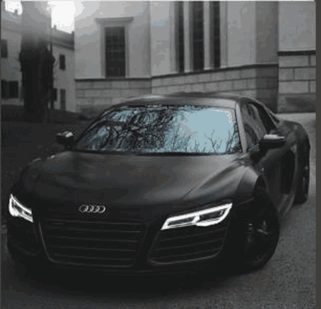 a black audi r8 coupe is parked in front of a building .