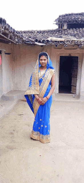 a woman in a blue and gold saree stands in front of a house