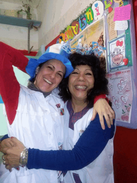 two women are hugging in front of a bulletin board that has a hello kitty on it