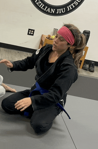 a woman kneeling on a mat in front of a brazilian jiu jitsu logo