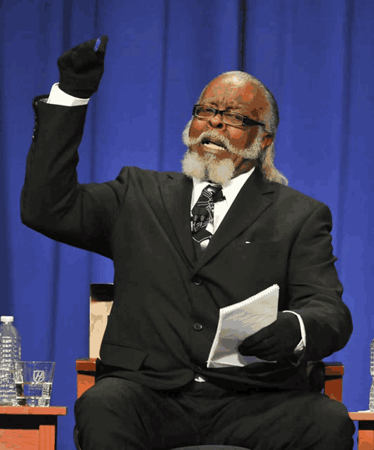 a man in a suit and tie is sitting in front of a blue curtain