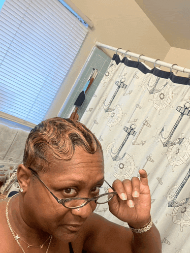 a woman wearing glasses in front of a shower curtain with anchors and steering wheels