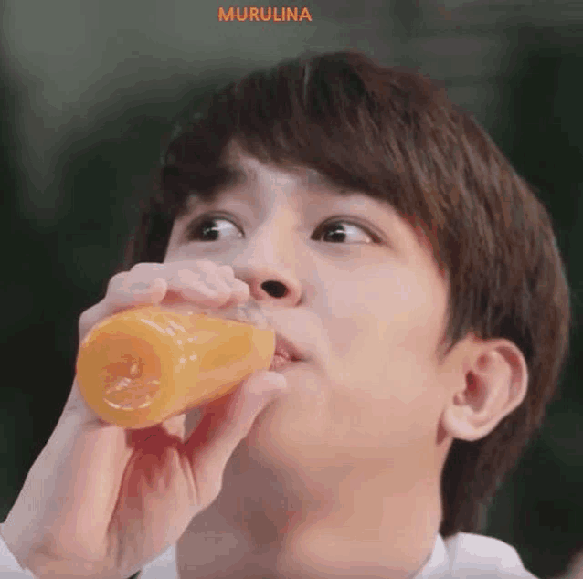 a man is drinking orange juice from a bottle .