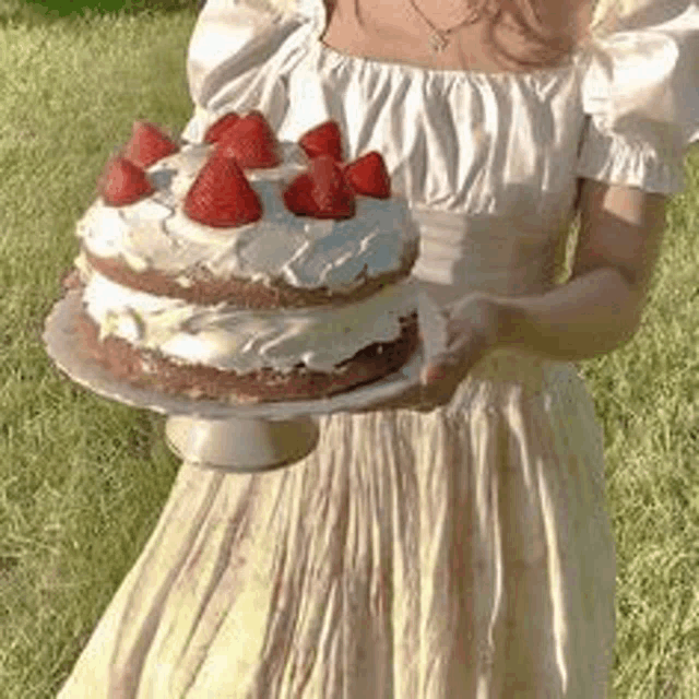 a woman in a dress is holding a cake with strawberries on top .