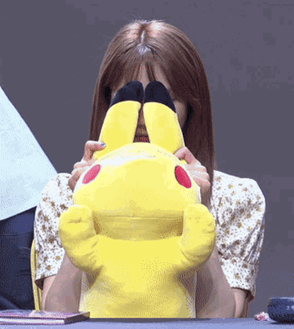 a woman covering her face with a yellow stuffed pikachu