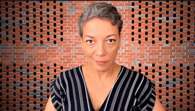 a woman stands in front of a brick wall wearing a black and white striped shirt