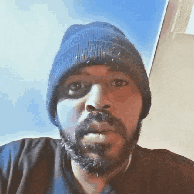 a man with a beard wearing a blue beanie looks at the camera