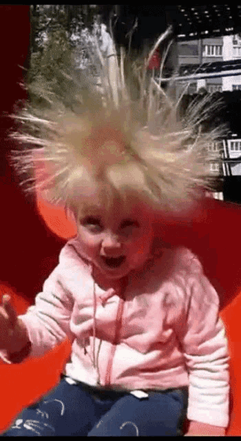 a little girl is sitting on a red slide with a bunch of static hair coming out of her head .