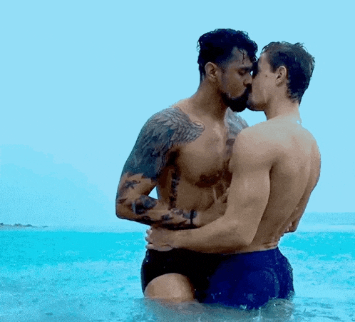 two men are kissing in the ocean while standing in the water .