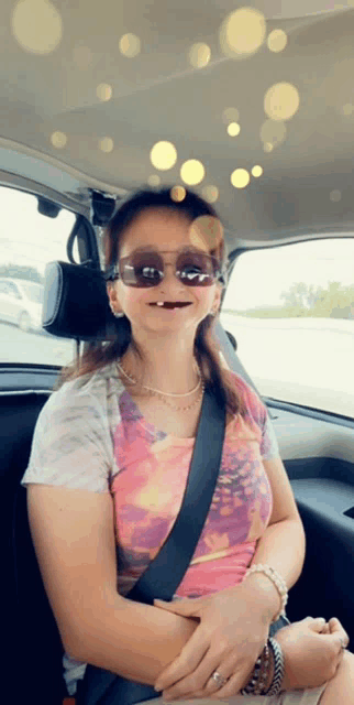 a woman wearing sunglasses and a pearl necklace is sitting in the back seat of a car