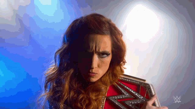 a woman is holding a wrestling belt with a w logo in the background