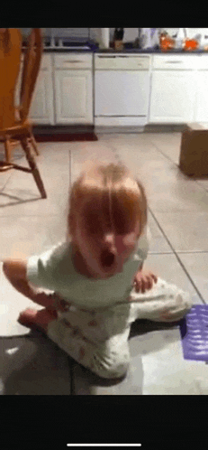 a little girl sitting on the floor with her mouth open