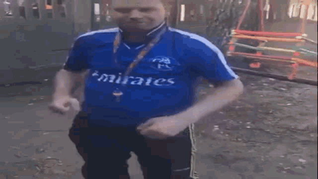 a man in a blue shirt is standing on a sidewalk with his arms outstretched in front of a playground .