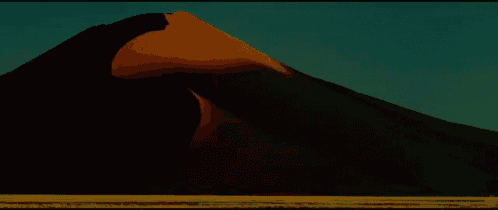 a large sand dune in the desert with a blue sky behind it