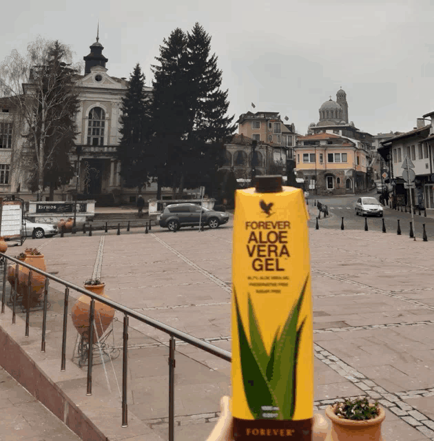 a person is holding a bottle of forever aloe vera gel in front of a city