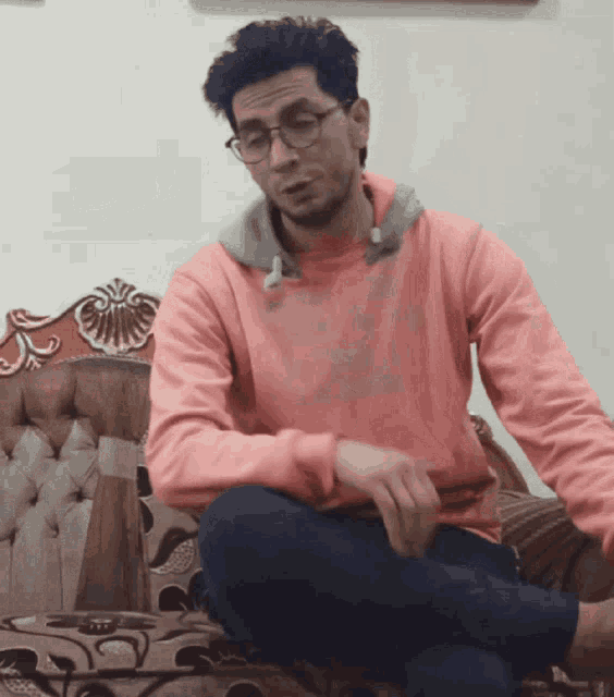 a man in a pink sweatshirt sits on a couch