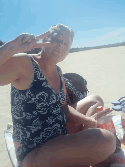 a woman in a bathing suit sitting on a beach with a coca cola bottle